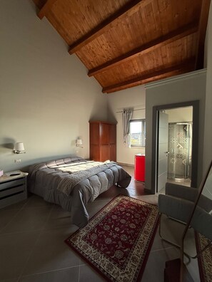 A bedroom with a bed, a nightstand, a lamp, a wardrobe, a red cabinet, a shower, and a patterned rug. - B & B Foresta Vini (Telese)