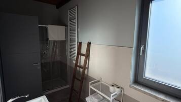 A bathroom with a shower, a sink, a towel rack, and a window.