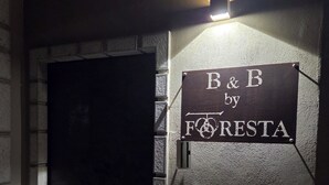 Ein an der Wand befestigtes Schild mit dem Schriftzug 'B&B by FORESTA', eine Tür und eine Wandleuchte.