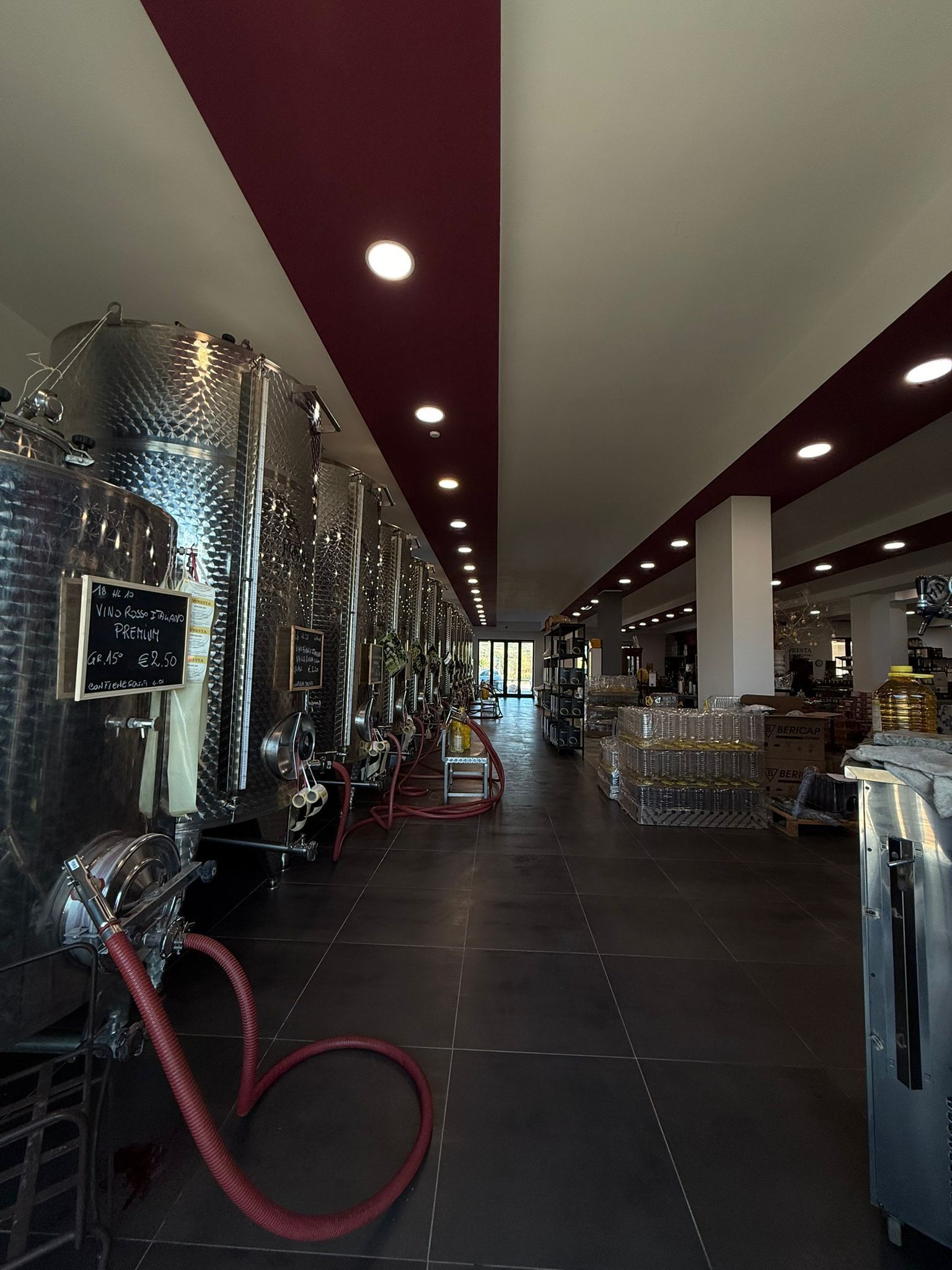 A wine cellar with stainless steel tanks, a chalkboard menu, and a red hose on the floor.