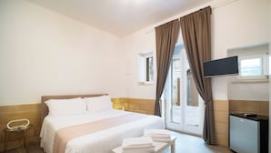 Ett hotellrum med en säng, ett litet bord med handdukar, en tv och ett litet kök.