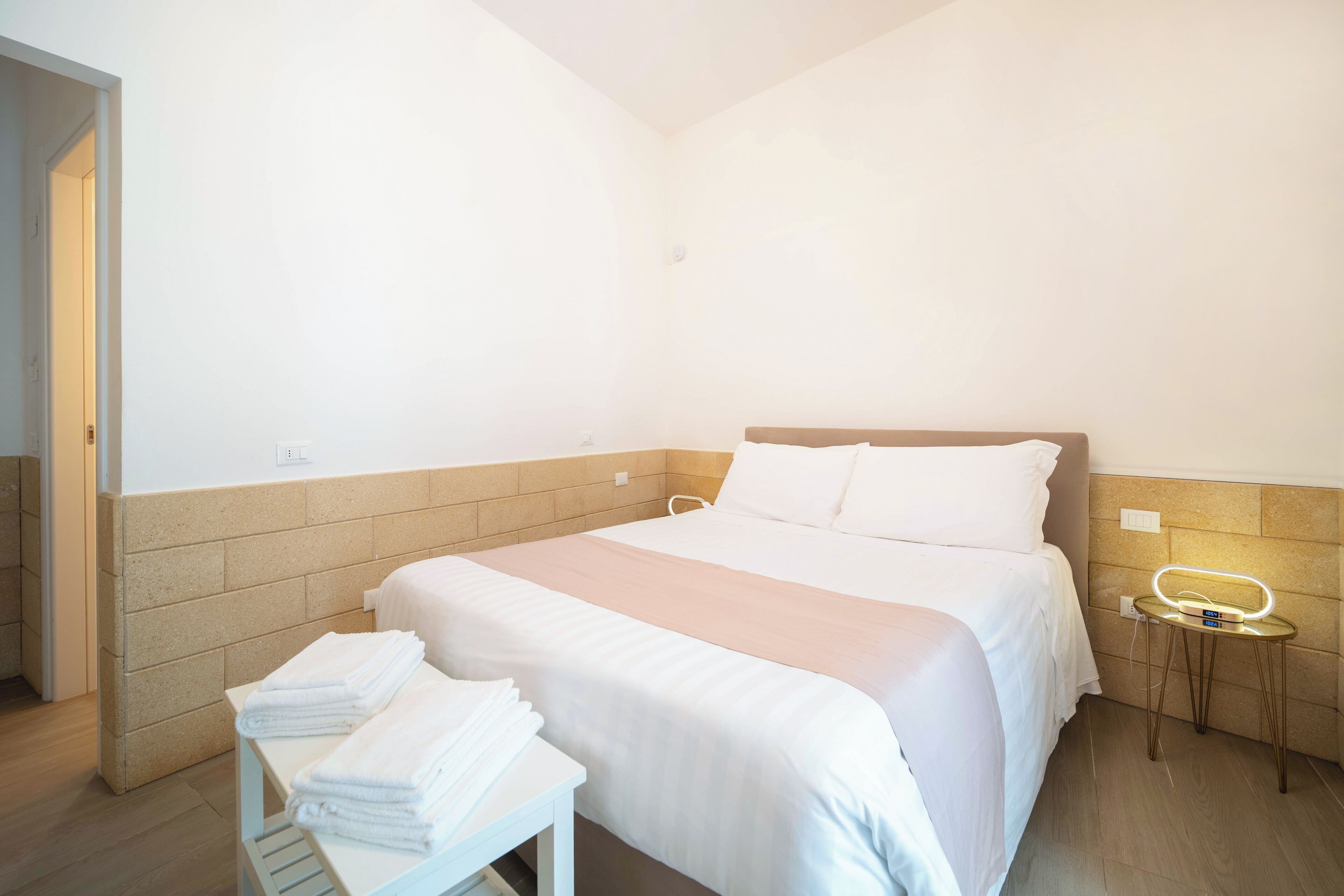 Een hotelkamer met een bed, een nachtkastje met handdoeken, een nachtlampje en een wandlamp.