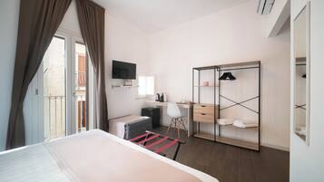 A hotel room with a bed, a desk, a chair, a wardrobe, and a television.