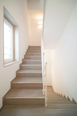 Una scala con gradini in legno e un corrimano, che conduce a una piattaforma con un lampadario.