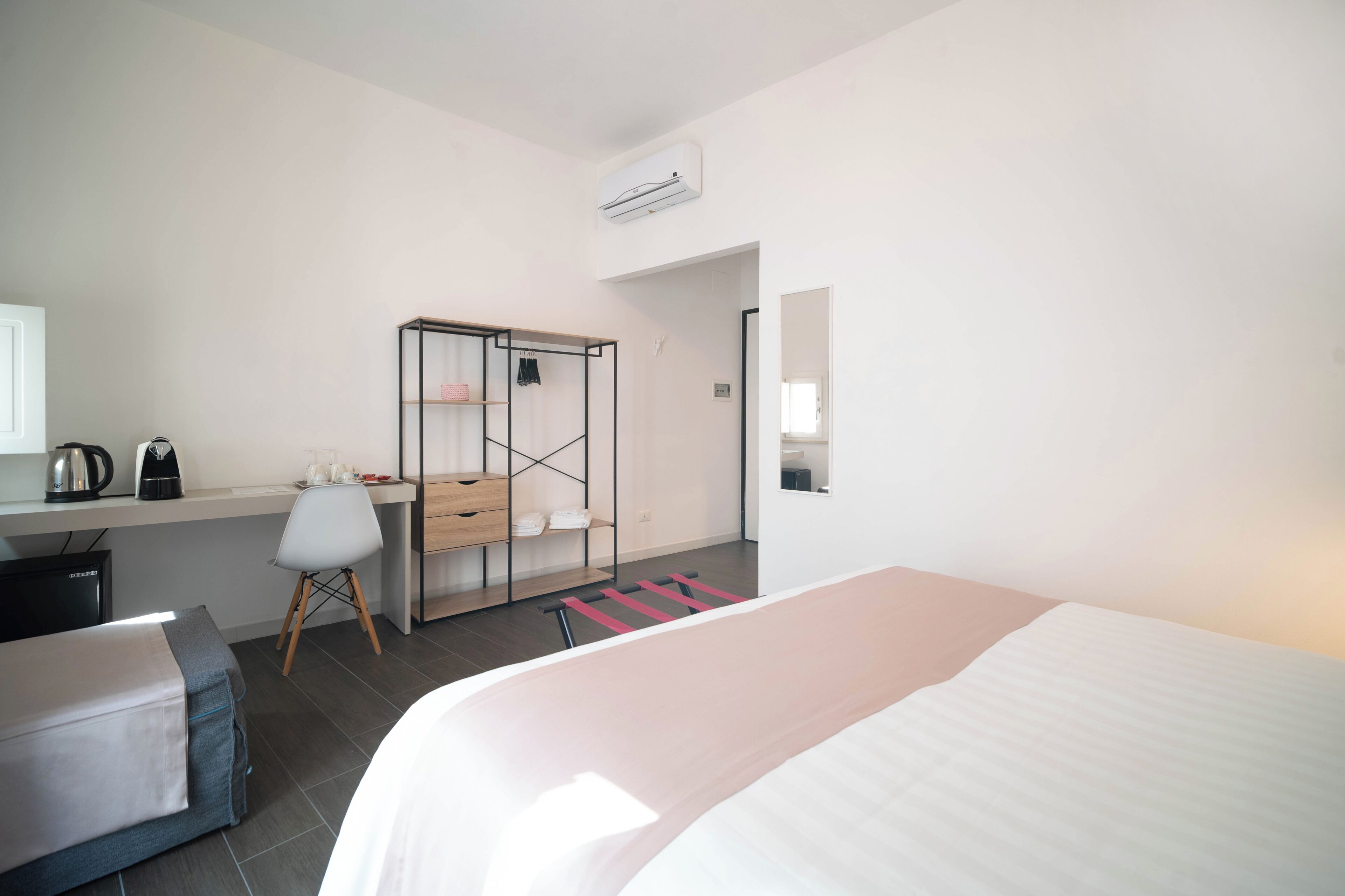 A hotel room with a bed, a desk with a chair, a wardrobe, and a mirror.