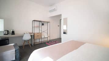A hotel room with a bed, a desk with a chair, a wardrobe, and a mirror.