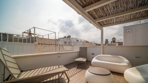 A rooftop terrace with a wooden deck, white lounge chairs, and a small table. - Le Contrade Vico Alba (Monopoli)