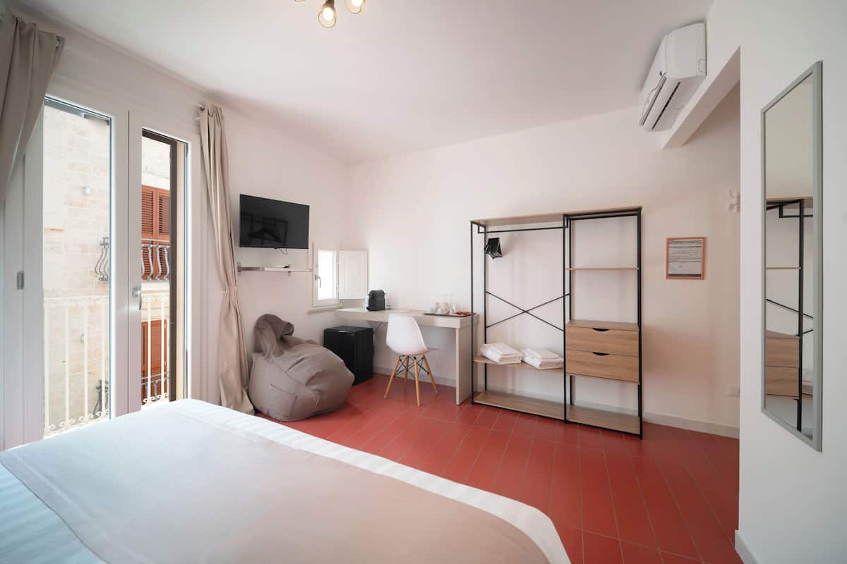 A bedroom with a bed, a desk, a chair, a wardrobe, and a balcony.