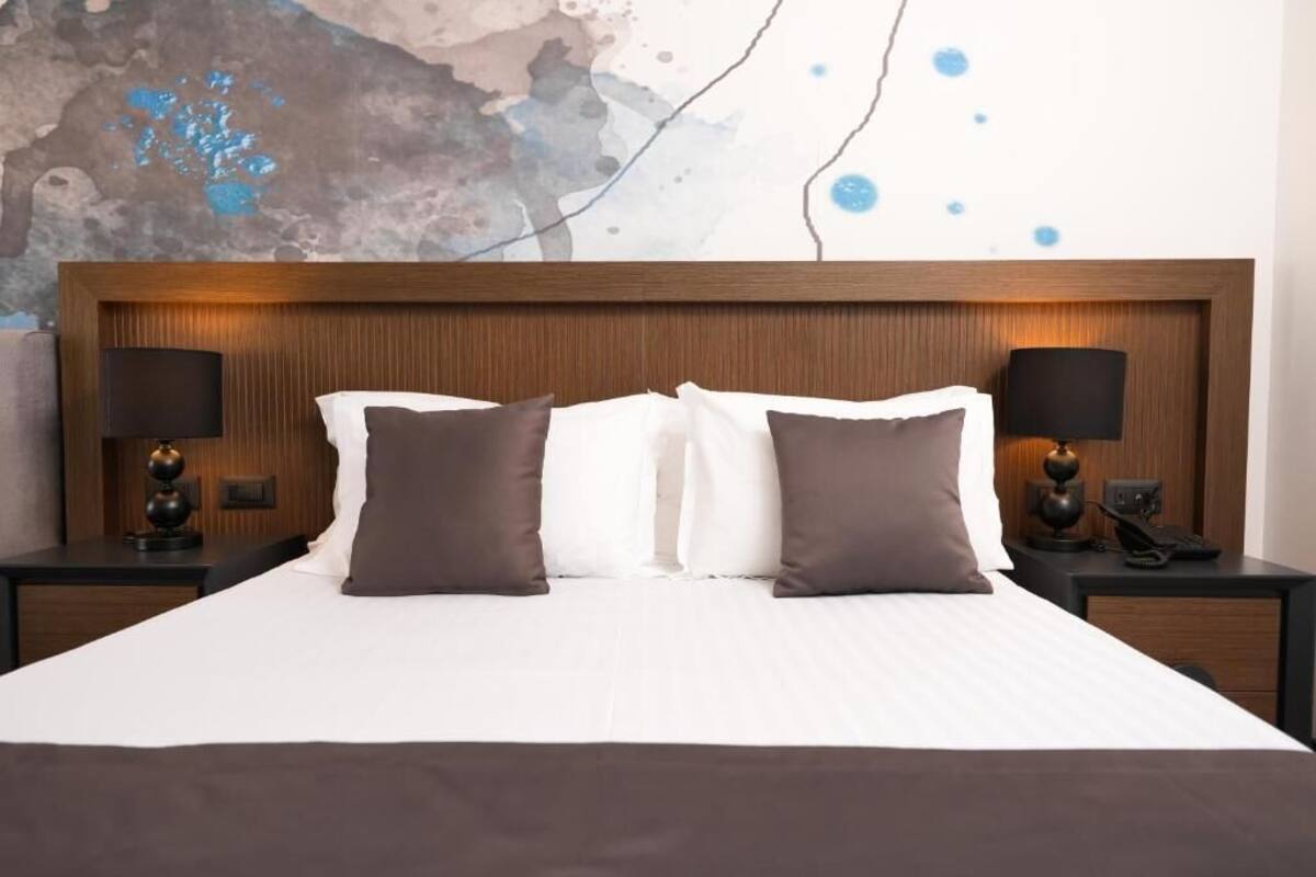 A hotel room with a large bed, two bedside tables with lamps, and a wall with a textured abstract design.