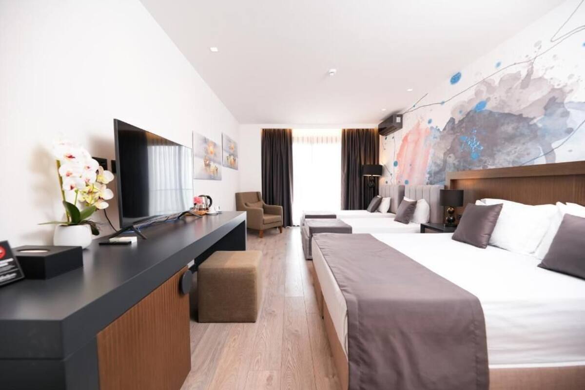 A hotel room with a bed, a desk, a chair, a TV, and a wall with abstract art.