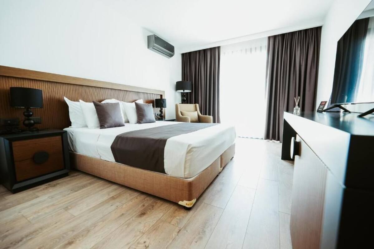 A hotel room with a bed, nightstand, chair, desk, and curtains.