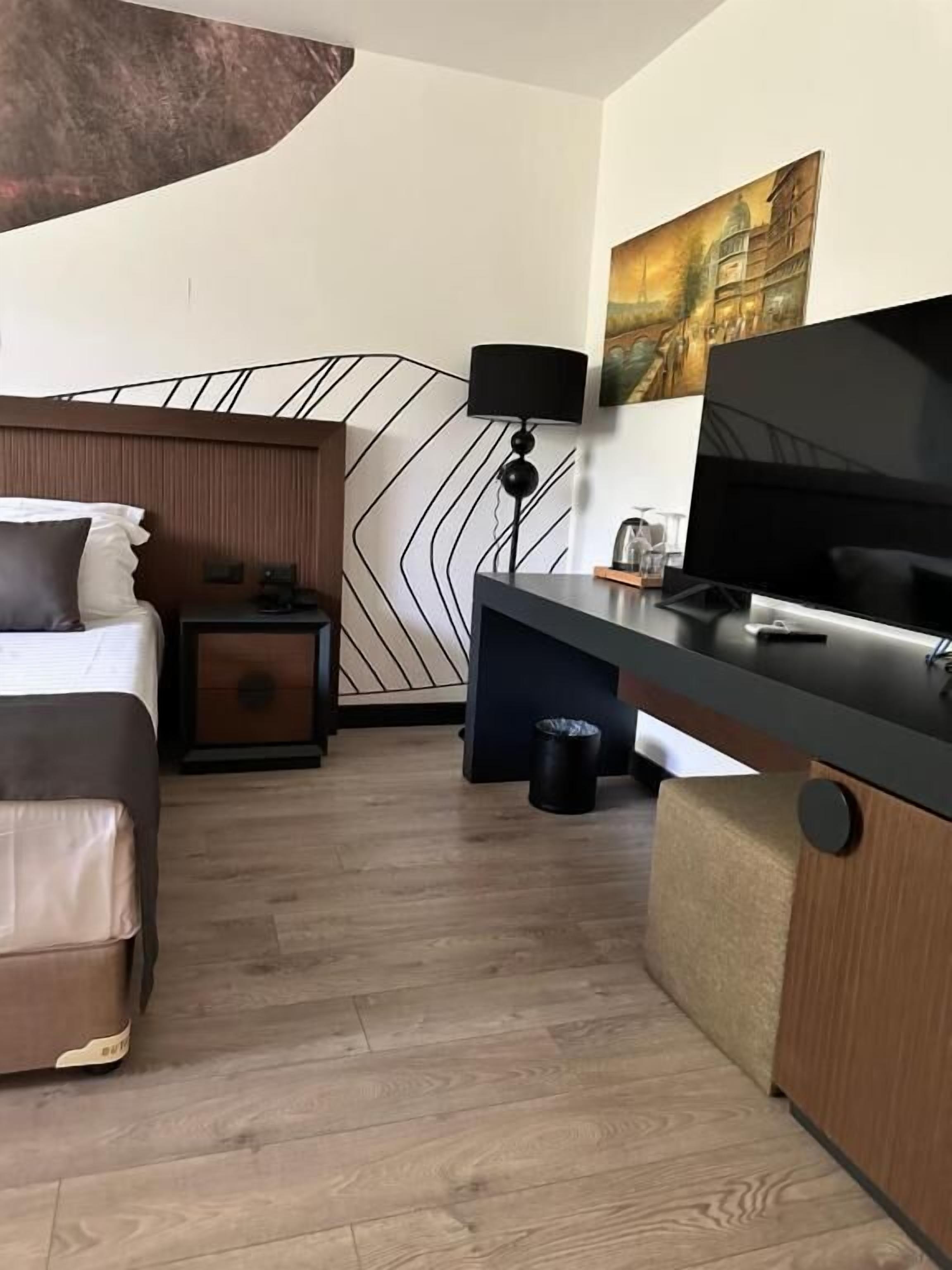 Una camera d'albergo con un letto, una scrivania con la TV, una lampada e un quadro appeso al muro.