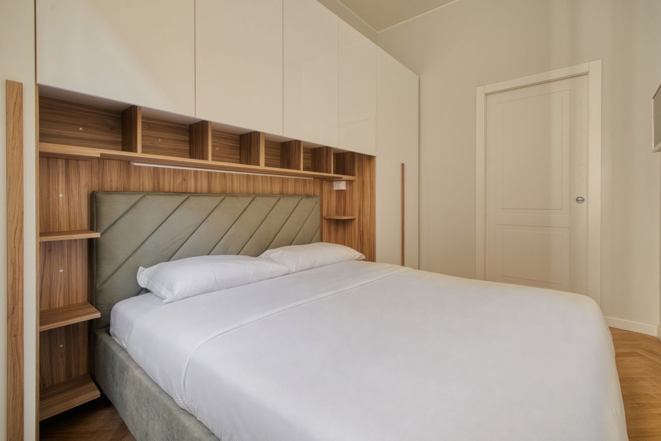 Een slaapkamer met een bed, houten hoofdeinde, inbouwkasten en een deur.