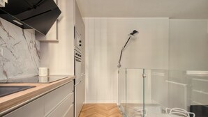Une cuisine moderne avec un pare-feu en marbre, un parquet en bois disposé en motif chevron et un coin repas vitré, agrémenté d’une table et de chaises blanches.