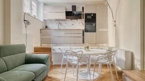 Une cuisine moderne avec des meubles blancs, un pare-feu en marbre et un coin repas comprenant une table et des chaises blanches.
