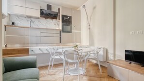 Une cuisine moderne avec des meubles blancs, un pare-feu en marbre et un coin repas comprenant des chaises blanches et une table ronde.