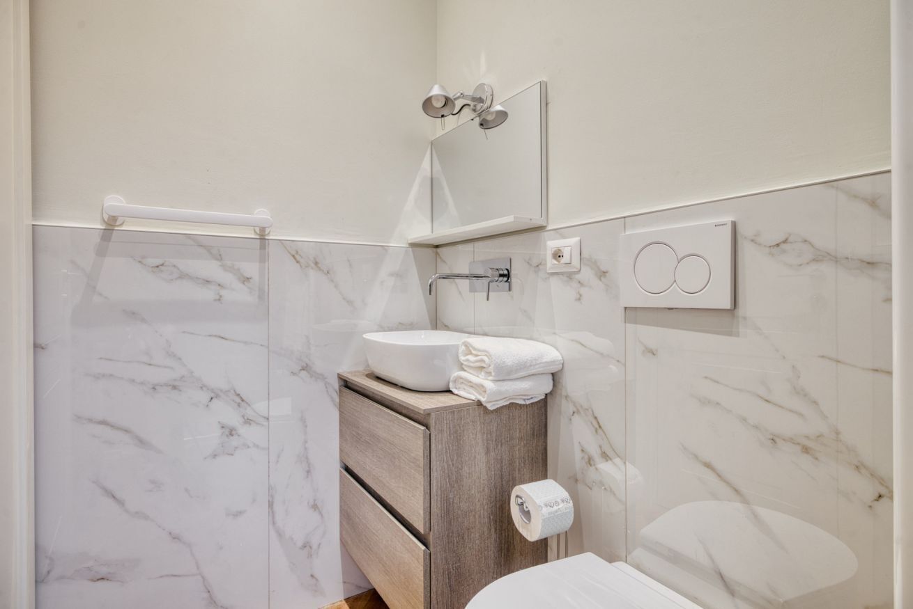A bathroom with a marble wall, a wooden vanity, a sink, a towel rack, a mirror, and a shower.