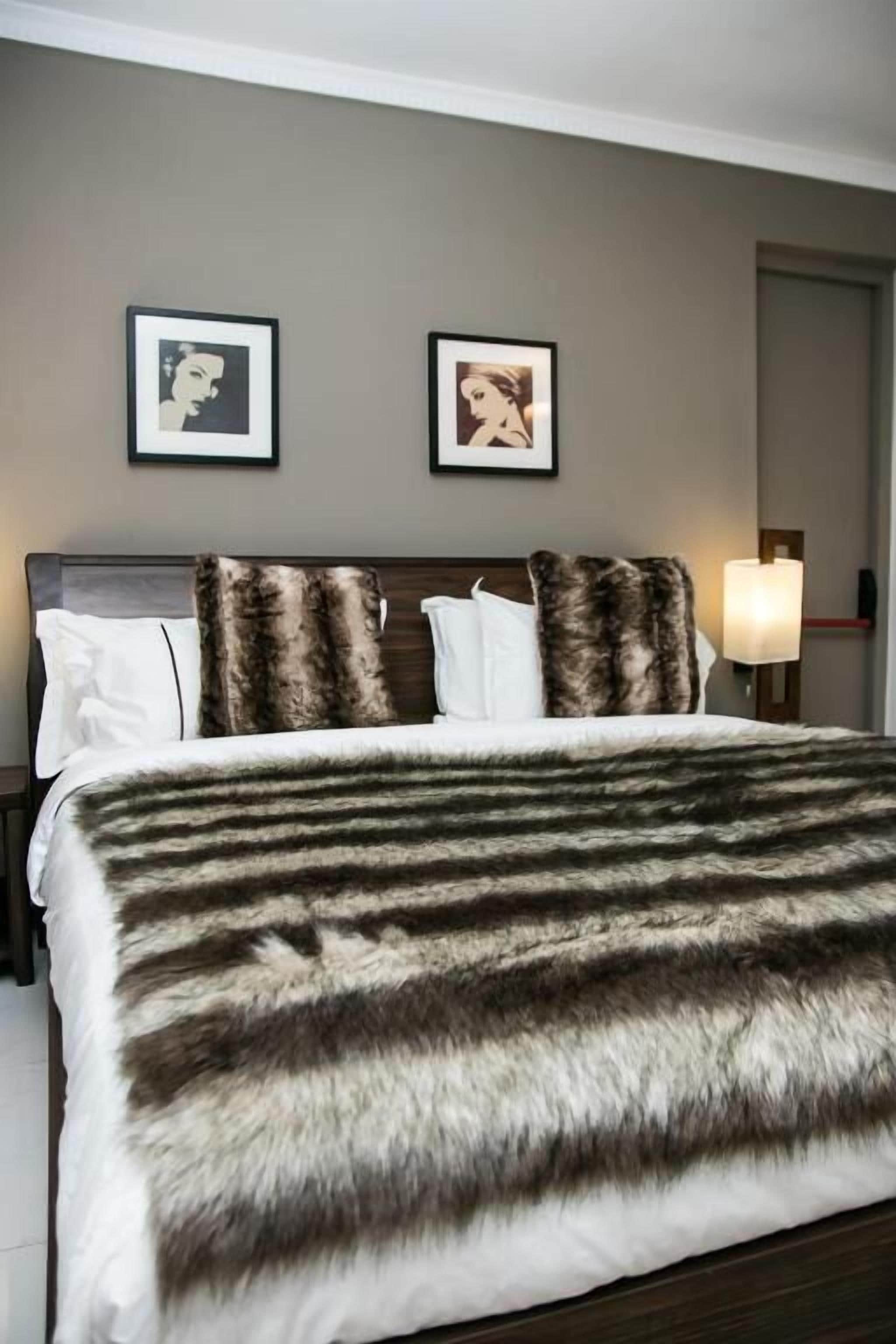 Une chambre d’hôtel avec un lit, deux tableaux encadrés au mur et une table de chevet avec une lampe.