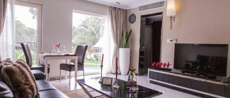 A modern living room with a sofa, a coffee table, a TV, and a dining area with a table and chairs.