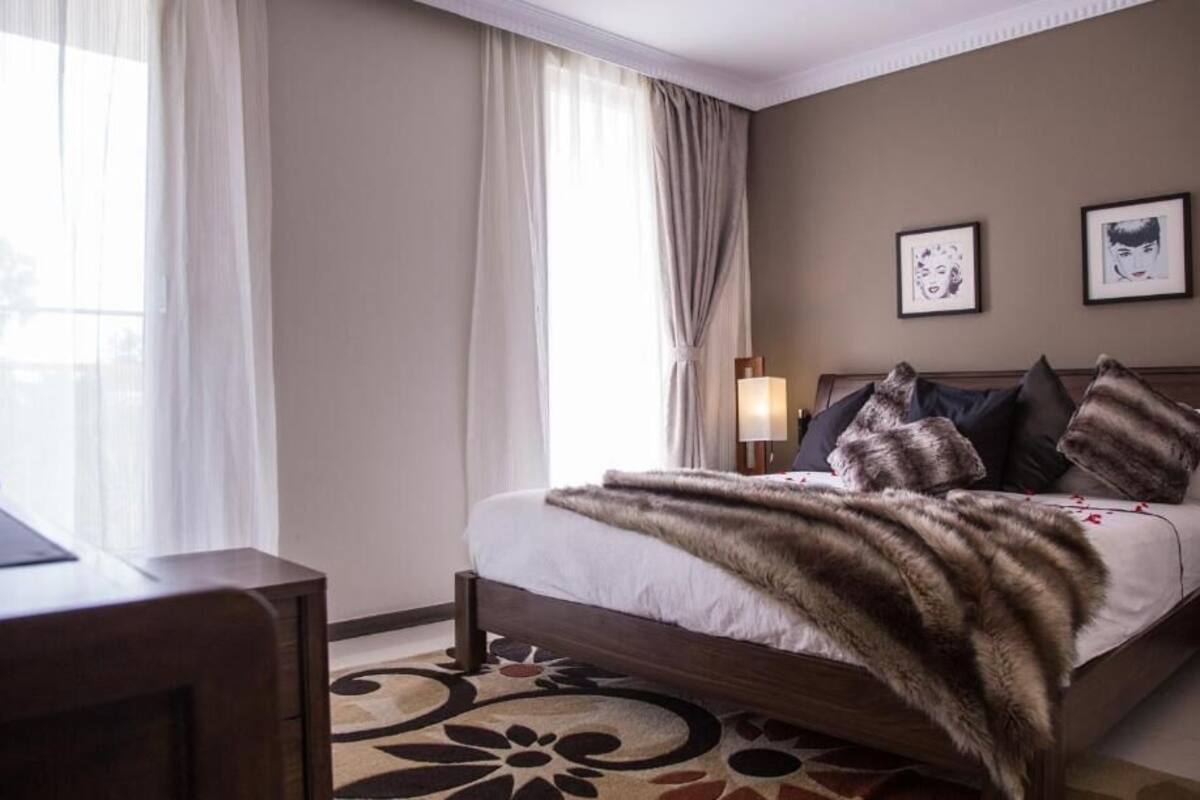 Una habitación de hotel con cama, cortinas, escritorio y cuadros en la pared.