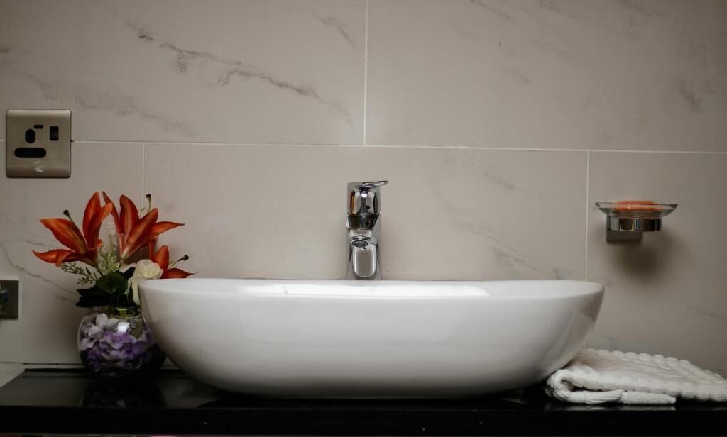A white sink with a modern faucet, a vase with flowers, and a towel on a black countertop.