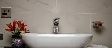 A white sink with a modern faucet, a vase with flowers, and a towel on a black countertop.