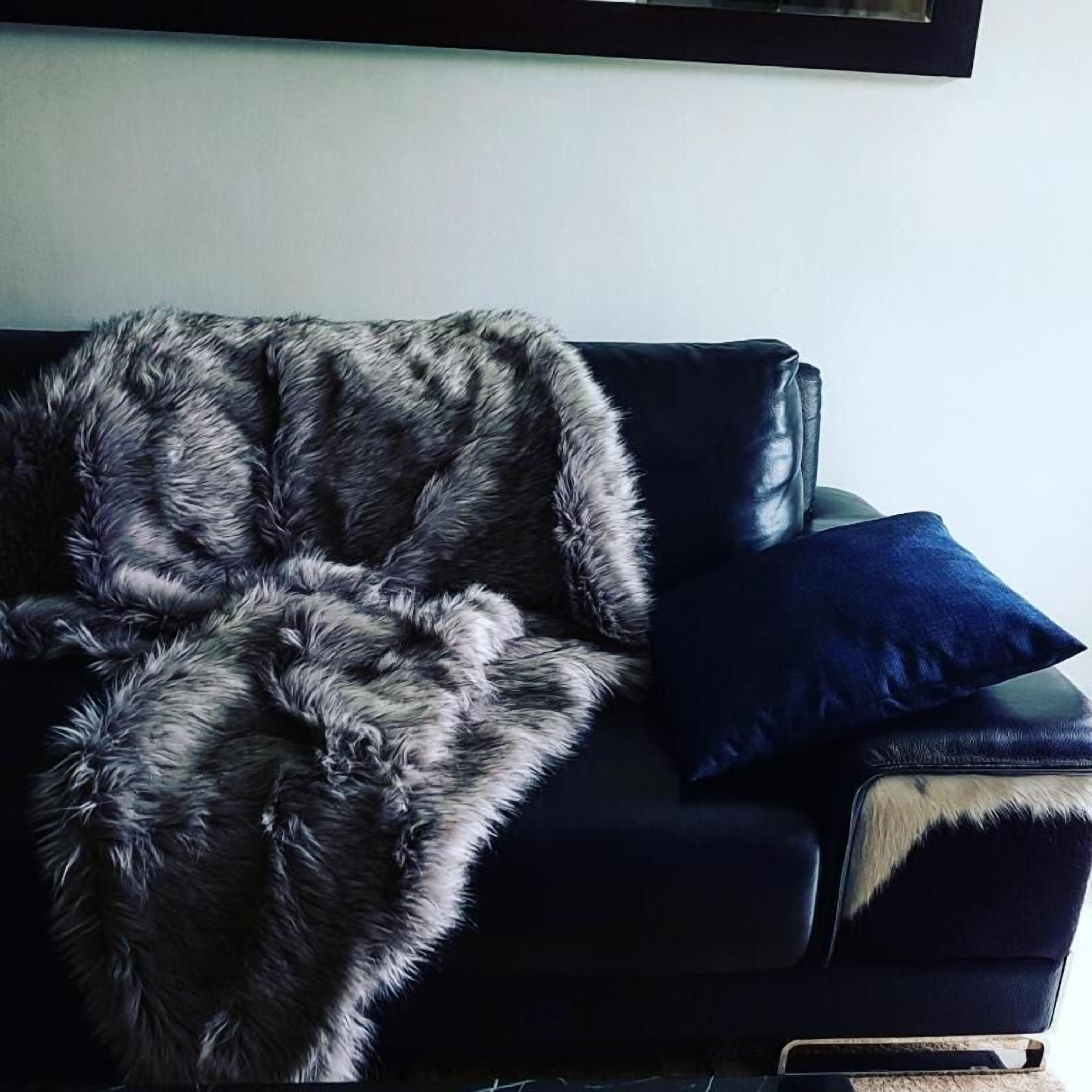 A dark leather sofa with a fur throw and a blue pillow.