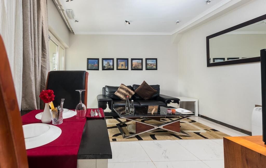 A living room with a red table set, a black leather sofa, and a coffee table with a geometric patterned rug.