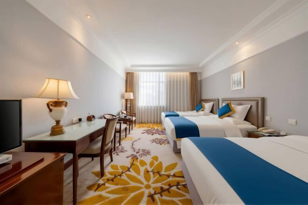 A hotel room with a bed, desk, chair, lamp, and a window with curtains.