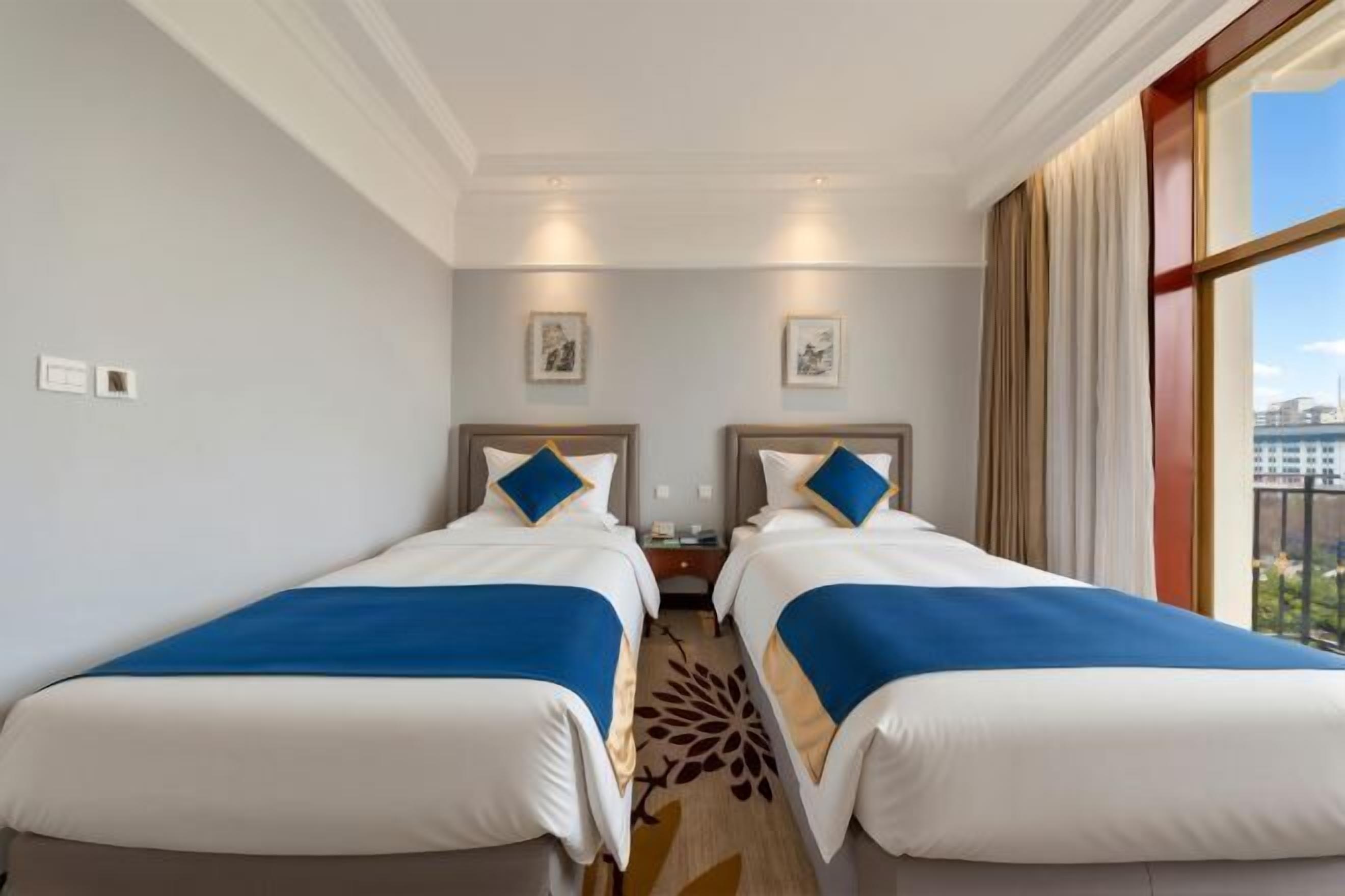 A hotel room with two beds, a large window, and a view of the city.