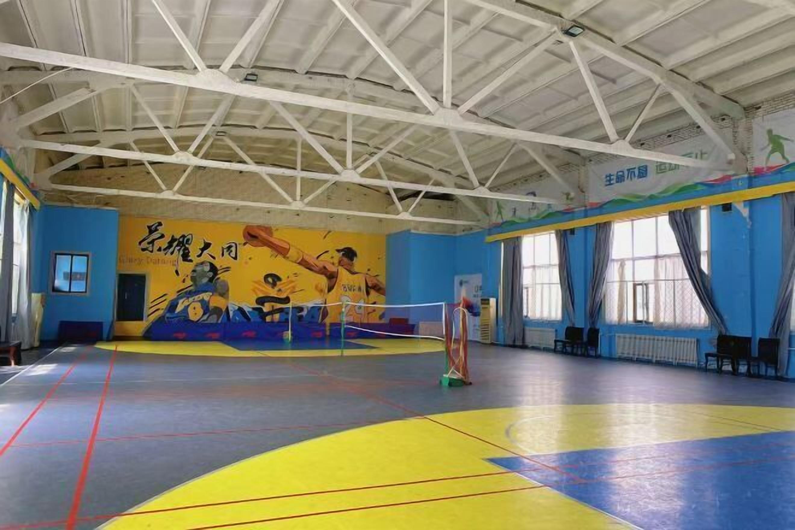 An indoor sports hall with a high ceiling, a volleyball net, and a mural on the wall.