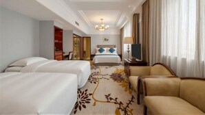 A hotel room with two beds, a sofa, a TV, and a chandelier.