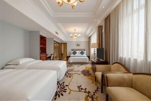 A hotel room with two beds, a sofa, a TV, and a chandelier.