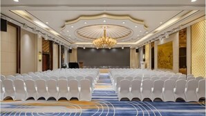 A conference room with rows of white chairs, a central stage, and a chandelier.