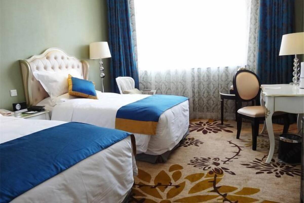 A hotel room with two beds, a desk, a chair, and a window with curtains.