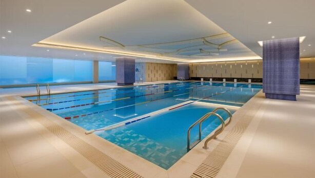A large indoor swimming pool with clear lanes, a diving board, and a modern ceiling design.