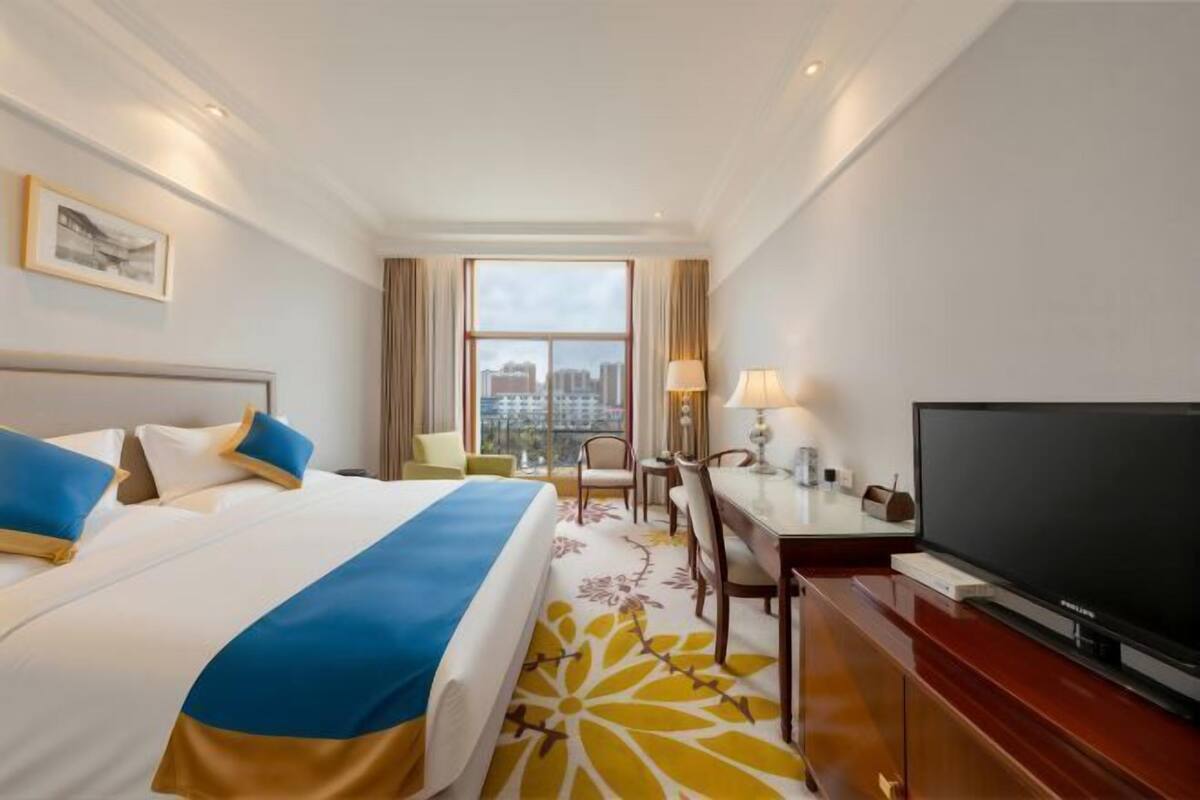 A hotel room with a bed, a desk, a television, and a window with a city view.