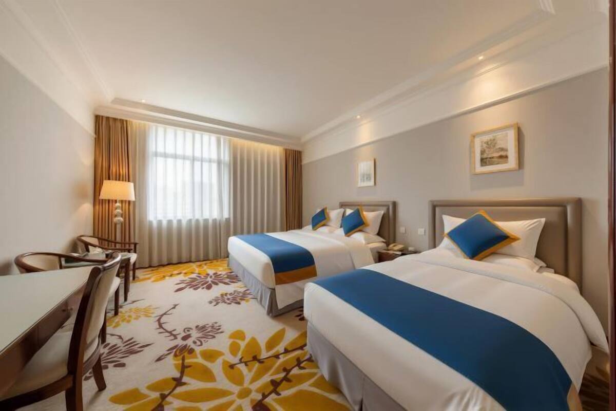 A hotel room with two beds, a desk, and a chair.
