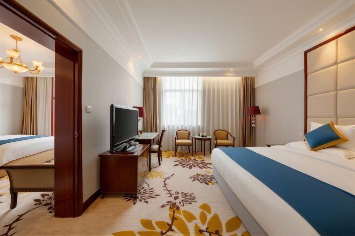 Une chambre d’hôtel comprenant un lit, un bureau avec une chaise, une télévision et une fenêtre avec des rideaux.
