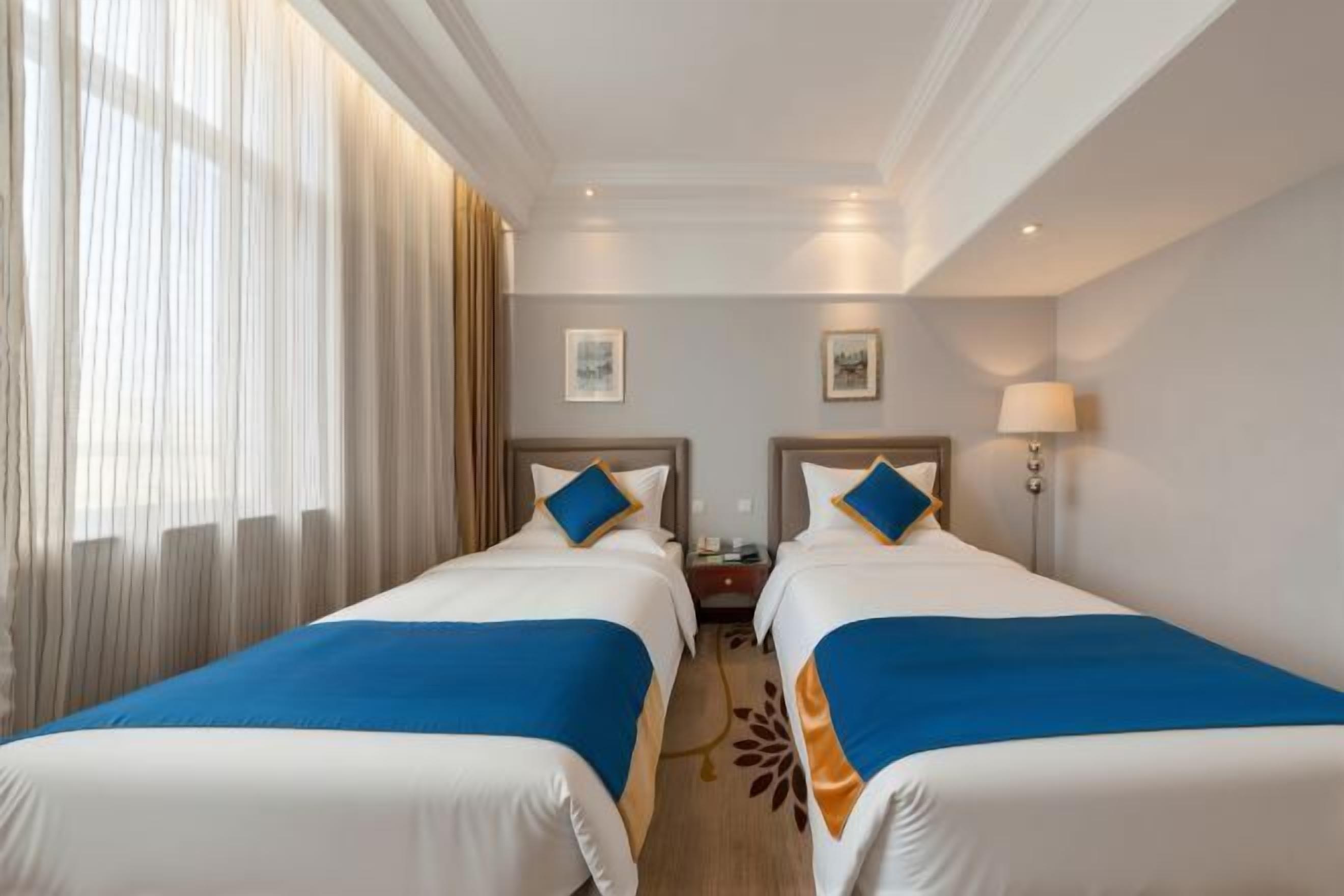 Una habitación de hotel con dos camas, una mesita de noche, una lámpara y una ventana con cortinas.