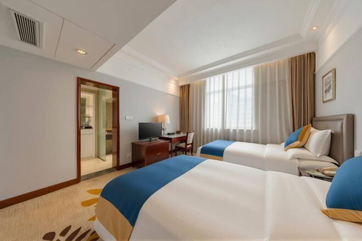 A hotel room with two beds, a desk with a chair, a television, and a window with curtains.