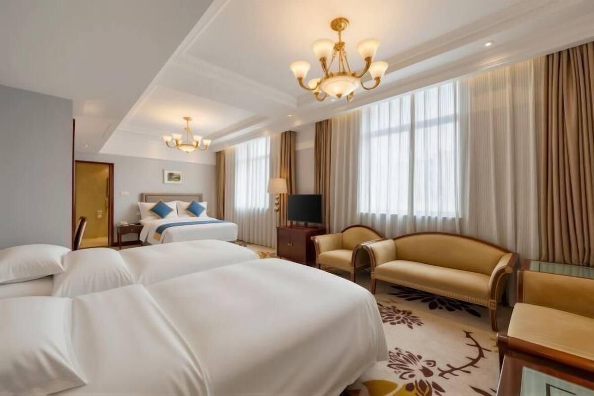 A hotel room with two beds, a sofa, a TV, and a chandelier.