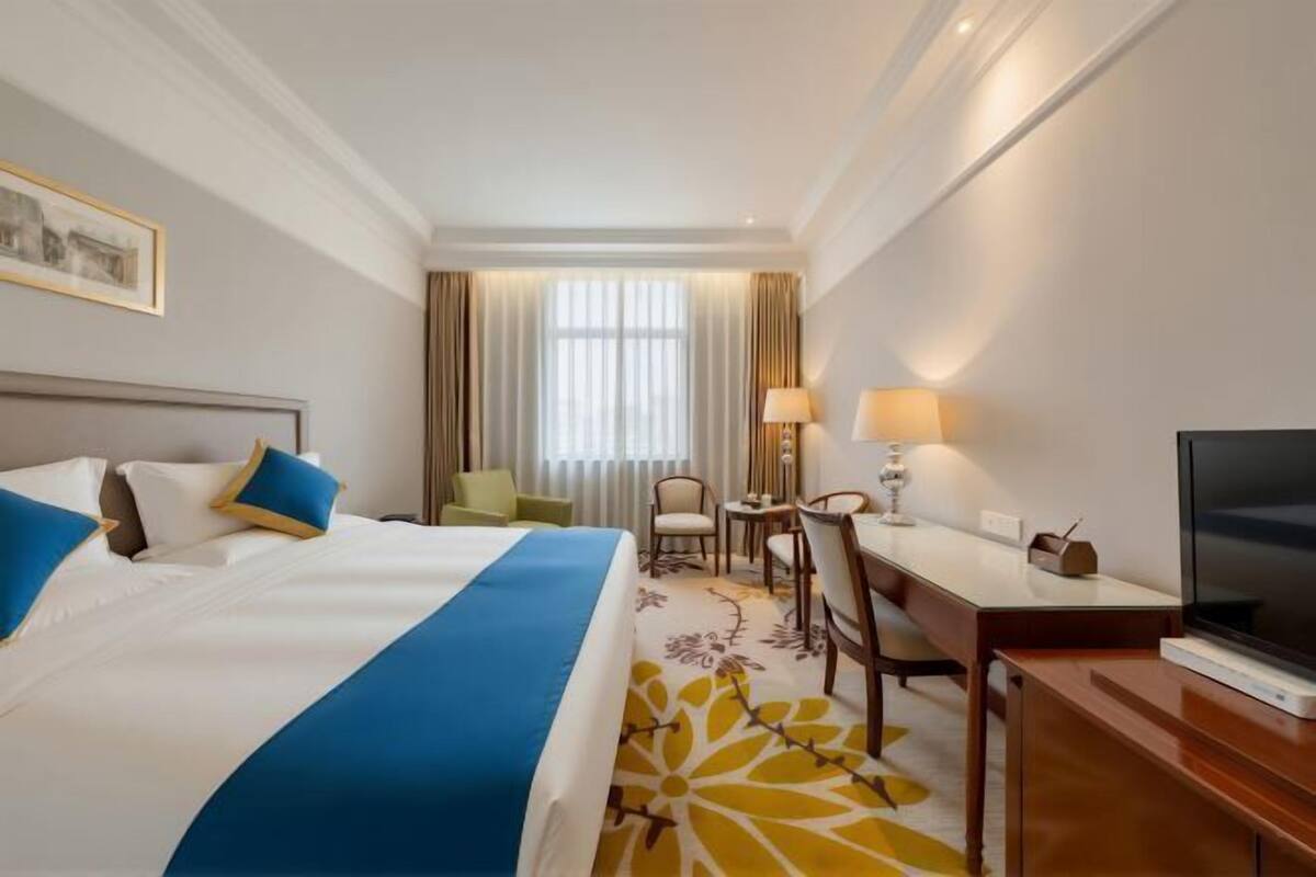 A hotel room with a bed, a desk, a chair, a television, and a window with curtains.
