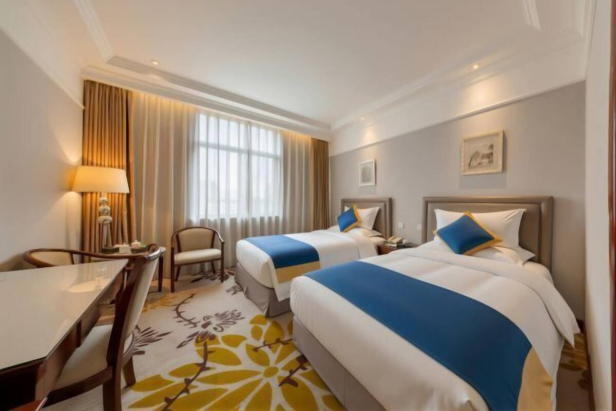 A hotel room with two beds, a desk, a chair, a lamp, and a window with curtains.