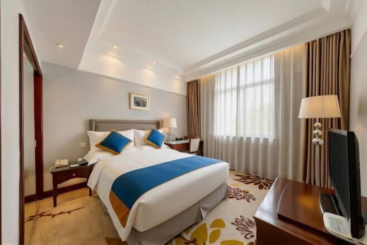 A hotel room with a bed, bedside tables, a desk with a computer, a TV, and a window with curtains.