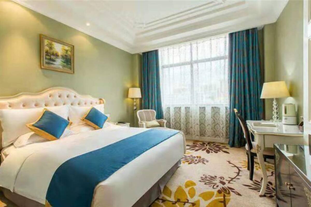 A hotel room with a large bed, a desk, a chair, and a window with curtains.