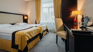 A hotel room with two beds, a desk with a lamp, and a chair.
