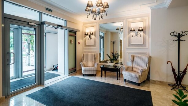 A hotel lobby with a reception desk, two striped armchairs, a chandelier, and a coat rack. - Optima Collection Chernihiv (Chernihiv)