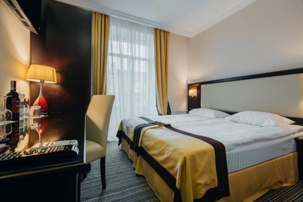 Habitación de hotel con cama, escritorio con lámpara, silla y televisión.