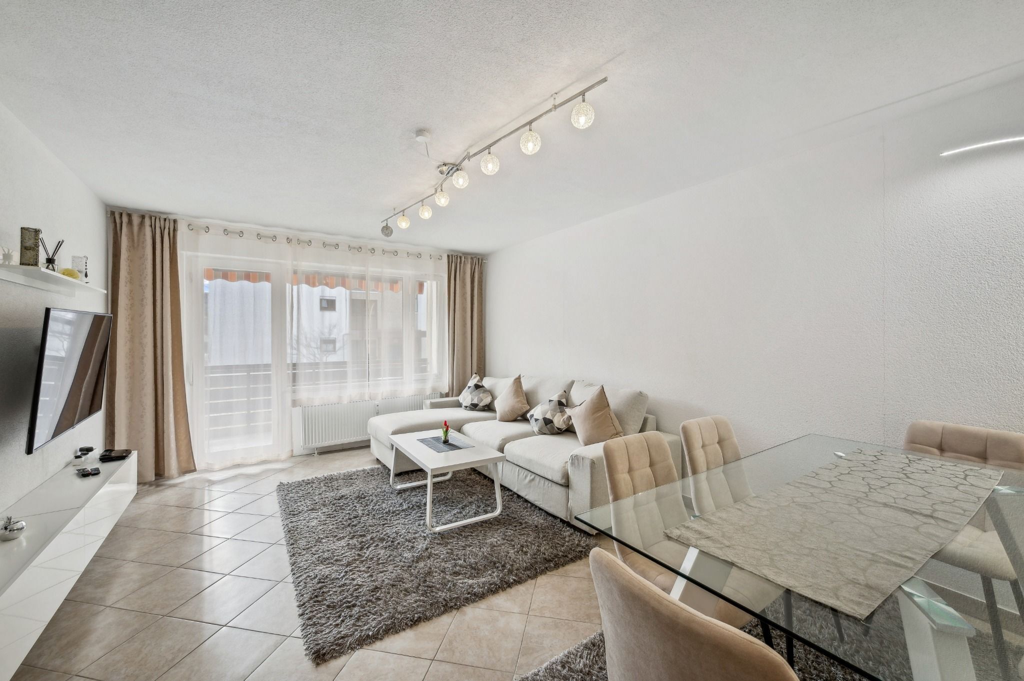 A modern living room with a sofa, a glass coffee table, a dining table, and a TV.